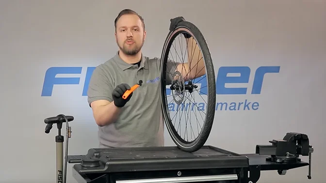 bike mechanic in front of Fischer logo, explaining bike tools and a wheel