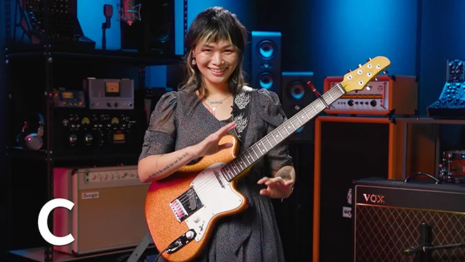 smiling woman, with an electric guitar, in her recording studio