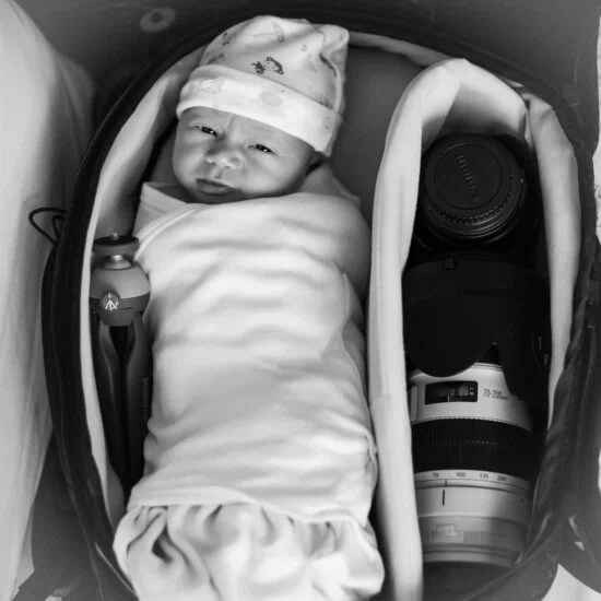 Baby in camera bag, lying next to a lense